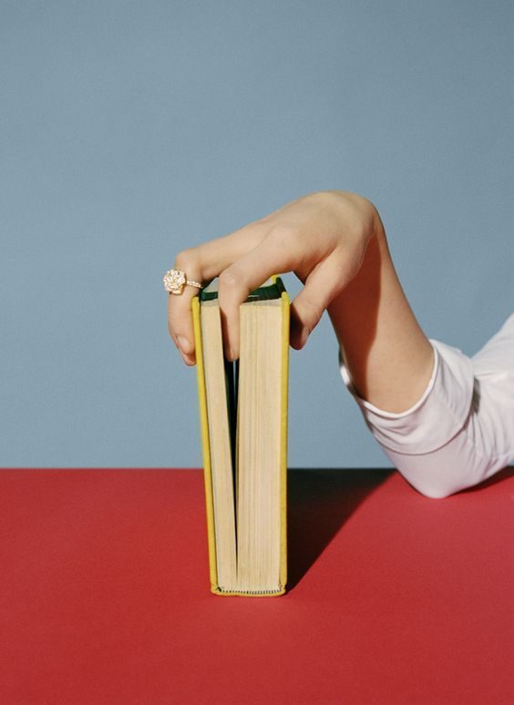 A hand balancing a book upright on a red table